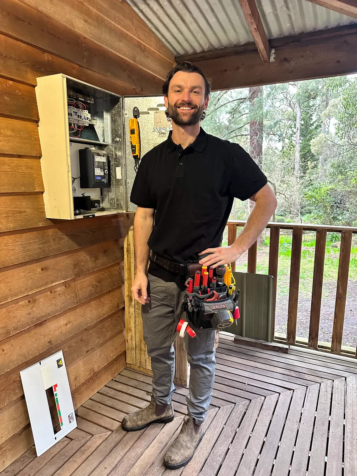 Kyle, owner electrician at TwentySix Electrical and Services, beside an open switchboard