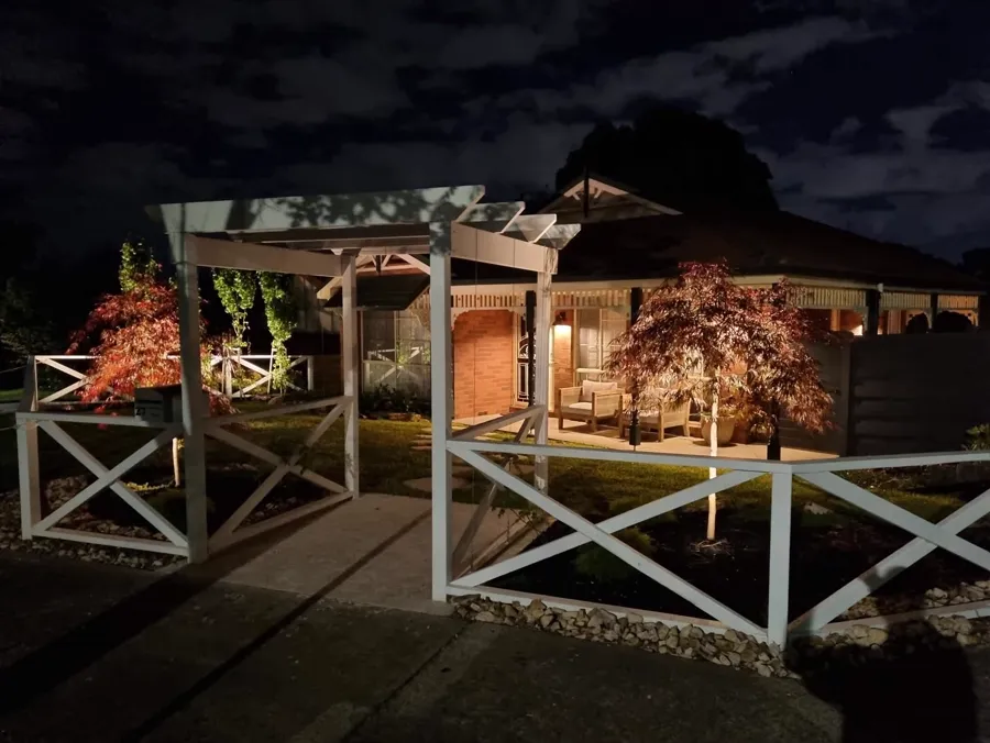 Weatherboard home with veranda, pergola and garden lighting at night